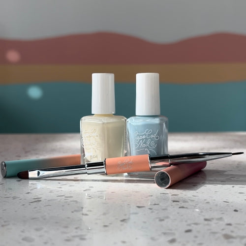 A professional manicure clean up brush, one end a flat oval, the other a short striper brush in Cape Cod Nail Co. colors on a marble countertop.
