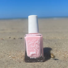 Load image into Gallery viewer, A bottle of pink nail polish on the sand with the ocean in the background.